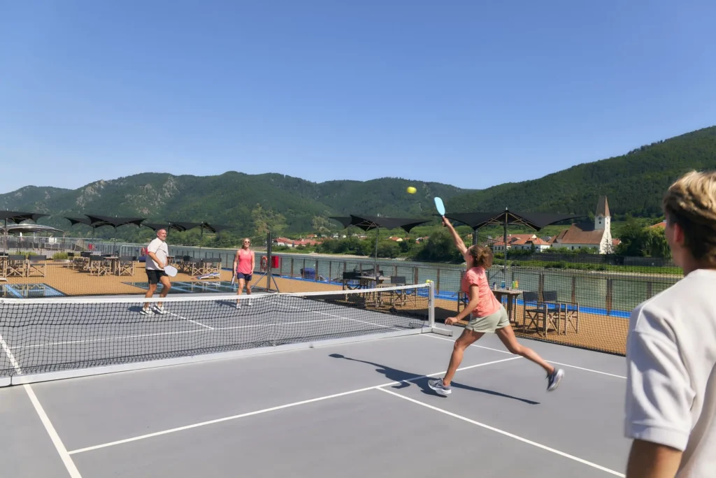 Guests playing pickleball on the sun deck of an AmaWaterways ship with mountains in the background
