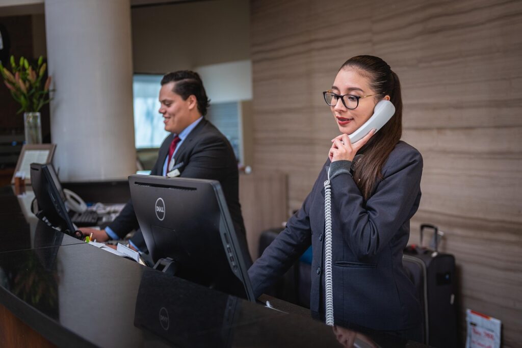 Two hotel receptionists at the front desk, one on the phone